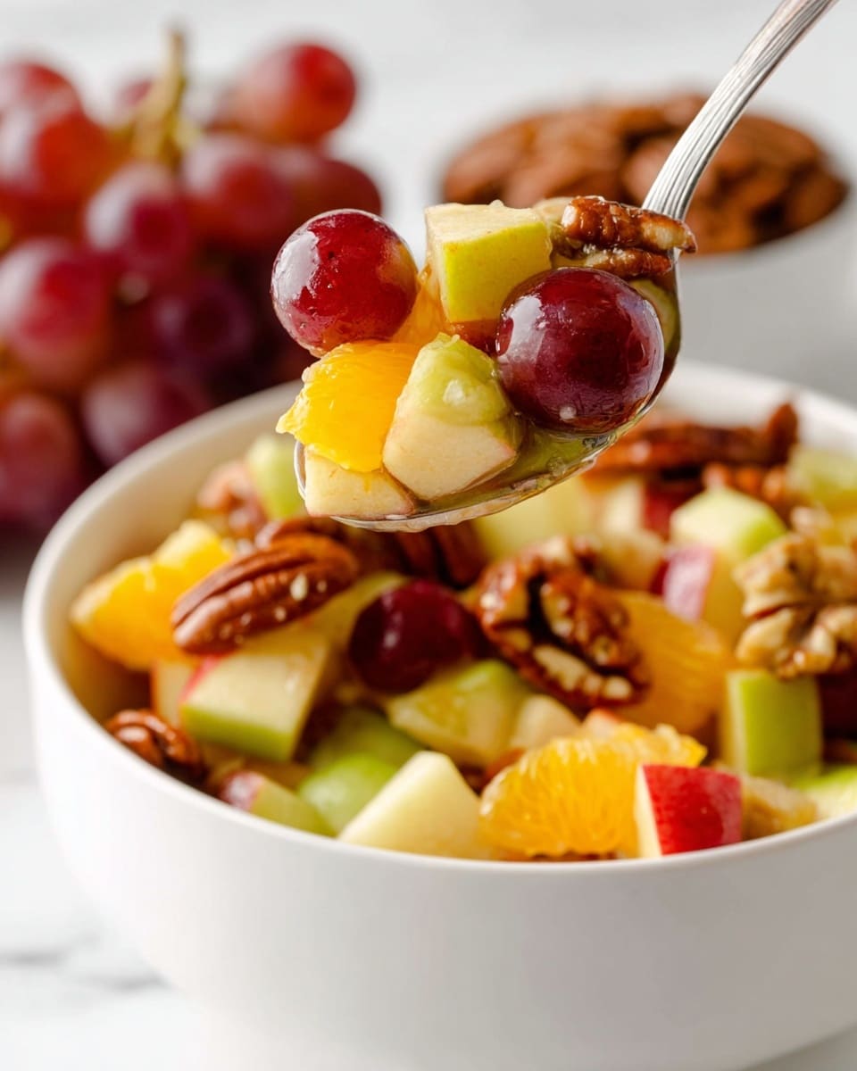 A white bowl filled with a colorful fruit salad showing three main layers: bottom layer of small red and green apple pieces with red skin and white flesh, middle layer with bright orange chunks of citrus fruit, and top layer with whole red grapes and glossy pecan nuts adding a textured brown touch. A spoon full of the same fruit and nut mix is held above the bowl with a bunch of red grapes and a small white bowl with pecans blurred in the white marbled background. The colors are vibrant and the textures range from smooth fruit skins to rough nut shells. photo taken with an iphone --ar 4:5 --v 7