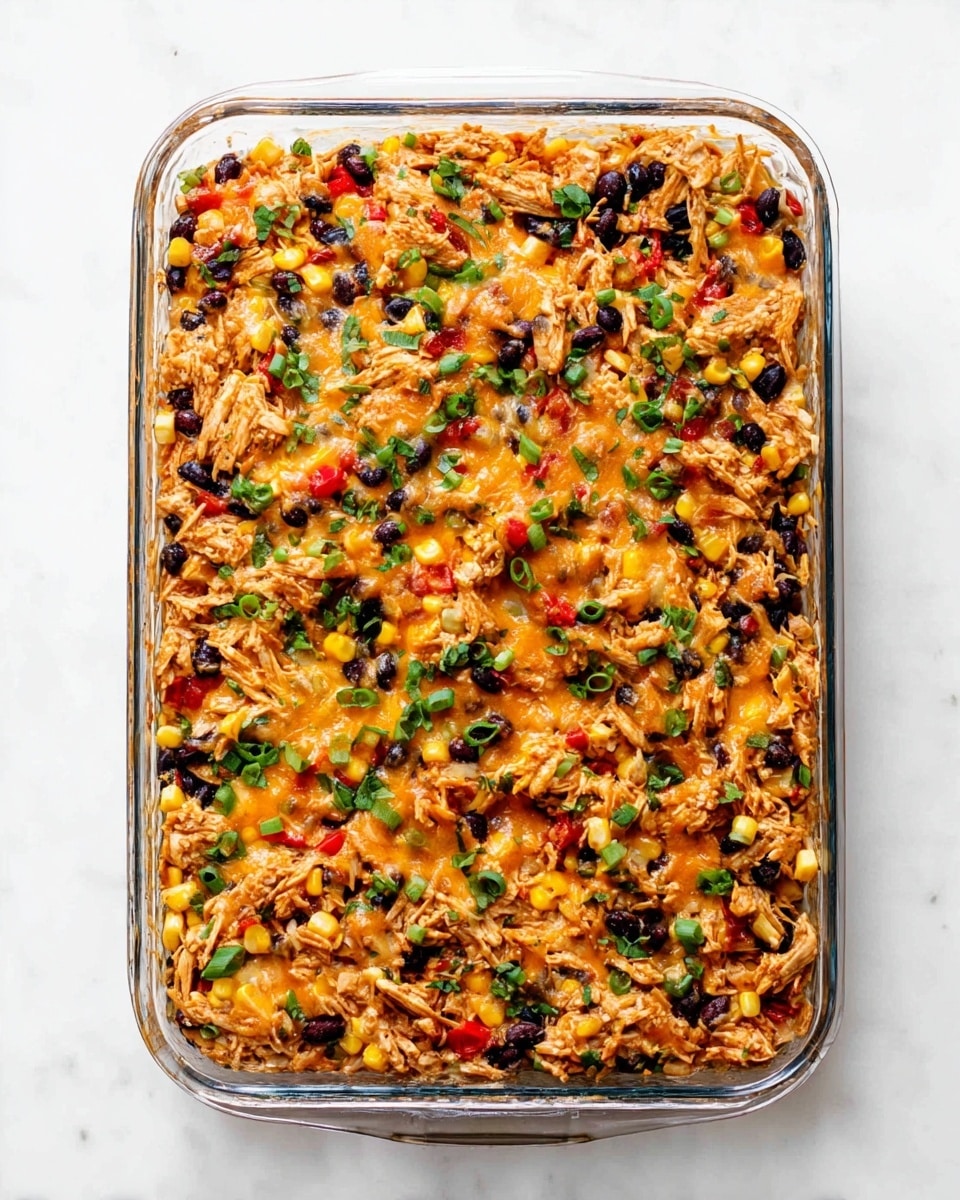 A clear glass rectangular dish filled with a layered casserole sits on a white marbled surface. The top layer is a mix of orange melted cheese, shredded light brown chicken, black beans, bright yellow corn kernels, small red pepper pieces, and green sliced spring onions, all evenly spread and slightly baked to golden brown edges. There are small bits of fresh green herbs sprinkled over the entire surface, adding a touch of freshness to the warm colors. The dish looks full and hearty, with a textured, colorful top layer that hints at a flavorful blend of ingredients. Photo taken with an iphone --ar 4:5 --v 7
