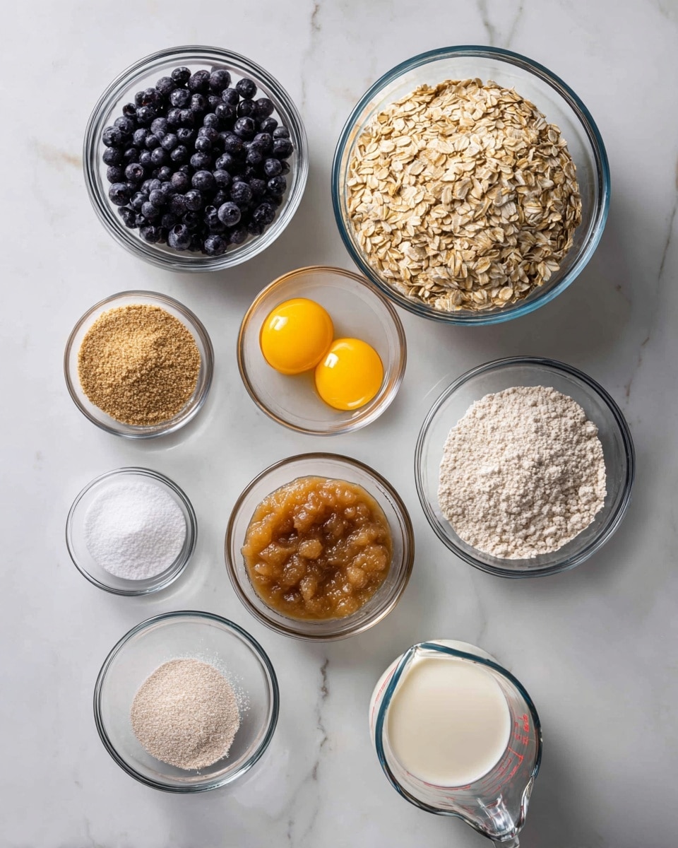 A top view shows nine clear glass bowls and a glass measuring cup, all placed on a white marbled surface. The largest bowl at the top right is filled with light brown rolled oats. To the left of it is a smaller bowl filled with dark blue blueberries. Below those, a bowl with three bright yellow egg yolks sits in the middle, and to its right, a bowl with light brown applesauce fills the space. Directly below, a glass measuring cup holds white milk. Surrounding these central bowls are smaller bowls containing white baking soda, light brown brown sugar, white baking powder, and white salt, creating a neat, organized layout. The photo taken with an iphone --ar 4:5 --v 7