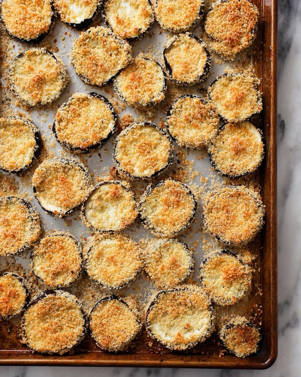 The image shows a baking tray filled with many round slices of eggplant coated in a golden brown breadcrumb layer. Each slice is about one layer thick, with the dark purple eggplant skin visible around the edges, giving a contrast to the light, crispy breadcrumb topping. The tray has some browned spots where the breadcrumbs have toasted more, and a few crumbs are scattered around the tray's surface. The background has a white marbled texture. photo taken with an iphone --ar 4:5 --v 7