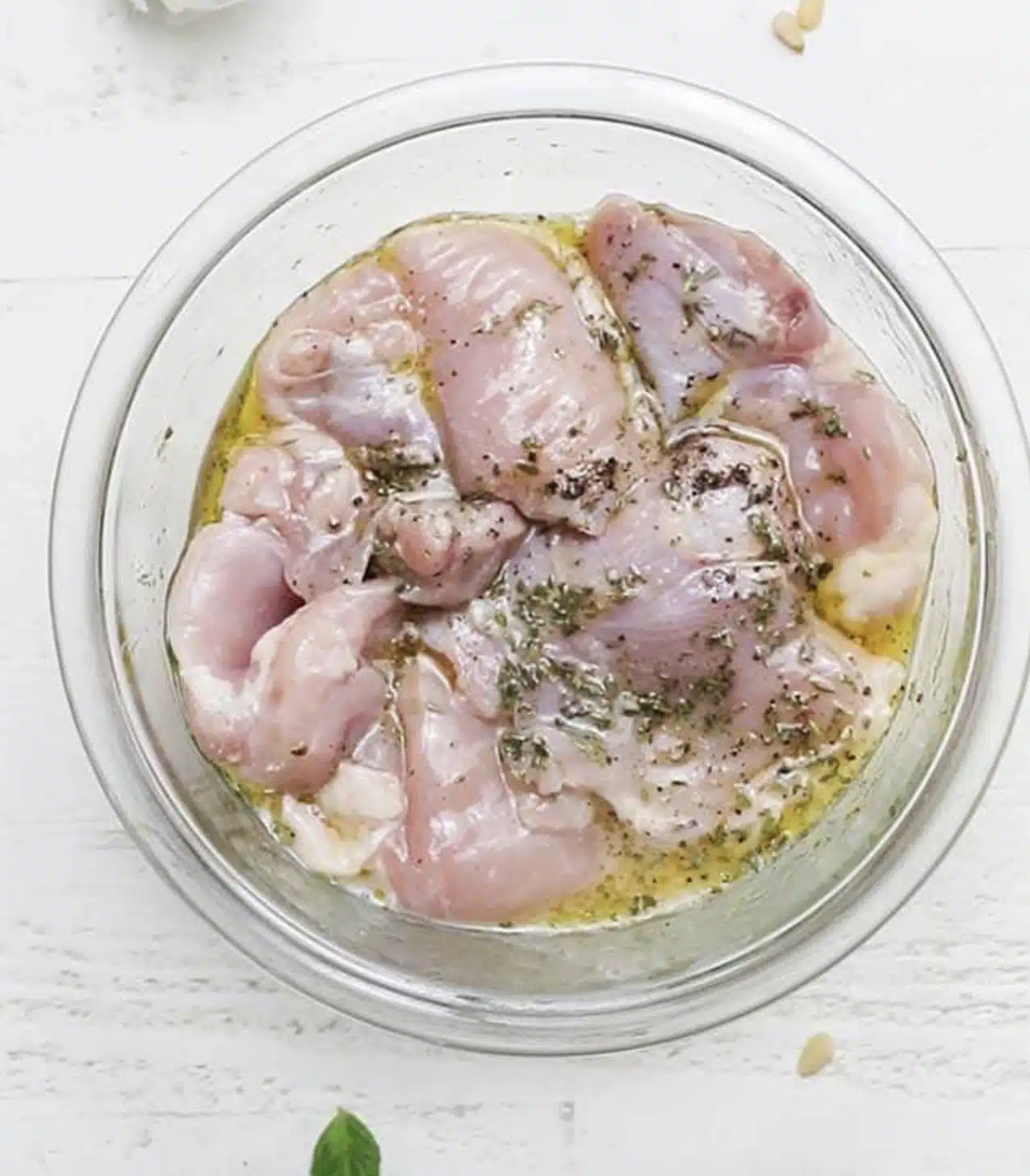 A close-up image shows several pieces of light pink raw chicken being sliced on a white cutting board placed on a white marbled surface. A pair of man's hands is visible, with one holding a knife cutting through a larger piece of chicken and the other stabilizing it. The chicken pieces are uneven in size, with some smaller chunks spread out in the lower part of the cutting board, and the raw meat's texture looks soft and moist. photo taken with an iphone --ar 4:5 --v 7