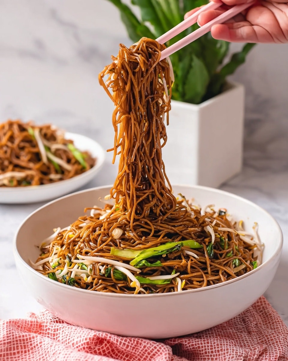 A white round bowl full of dark brown noodles mixed with light beige bean sprouts and some bright green leafy vegetables. A woman's hand with light skin tone is using light pink chopsticks to lift a large cluster of noodles high above the bowl, showing the thin, slightly shiny strands. The bowl sits on a white marbled surface, with another white bowl of the same noodles slightly blurred in the background. A small green potted plant in a white square pot adds color behind the bowl. A pink and white checkered cloth is folded in front of the bowl. photo taken with an iphone --ar 4:5 --v 7