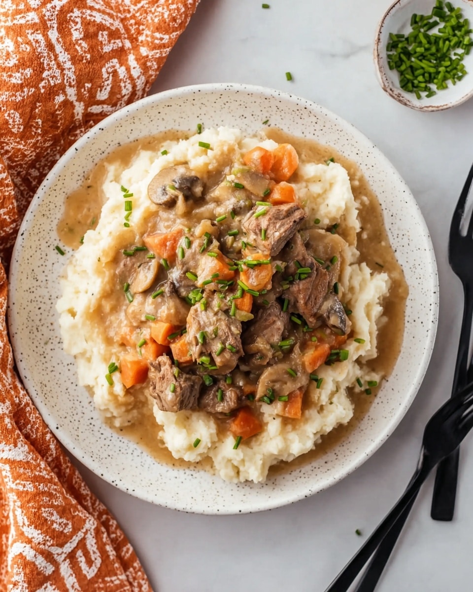 The dish is served on a white speckled plate placed on a white marbled surface. The bottom layer consists of creamy mashed potatoes, soft and slightly textured, forming a thick round bed. On top, there is a thick stew-like layer with chunks of tender brown meat, small orange carrot pieces, and bits of mushroom in a light brown sauce. The dish is finished with green chopped chives sprinkled evenly on the top and around the edges on the mashed potatoes. To the side, two black forks are placed next to the plate, and an orange and white patterned cloth is partially visible. photo taken with an iphone --ar 4:5 --v 7
