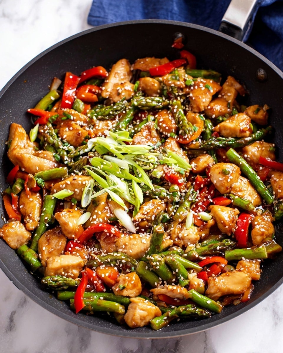 The image shows a black frying pan filled with a colorful stir-fry dish. The dish has several layers: golden-brown cooked chicken pieces scattered throughout, bright green asparagus segments cut in small pieces, and red bell pepper strips that add vibrant color. The ingredients are coated lightly with a shiny brown sauce. On top, there are fresh, thin slices of green onions and a sprinkling of white sesame seeds, adding texture and contrast. The frying pan is set on a white marbled surface with a blue cloth visible in the background. photo taken with an iphone --ar 4:5 --v 7