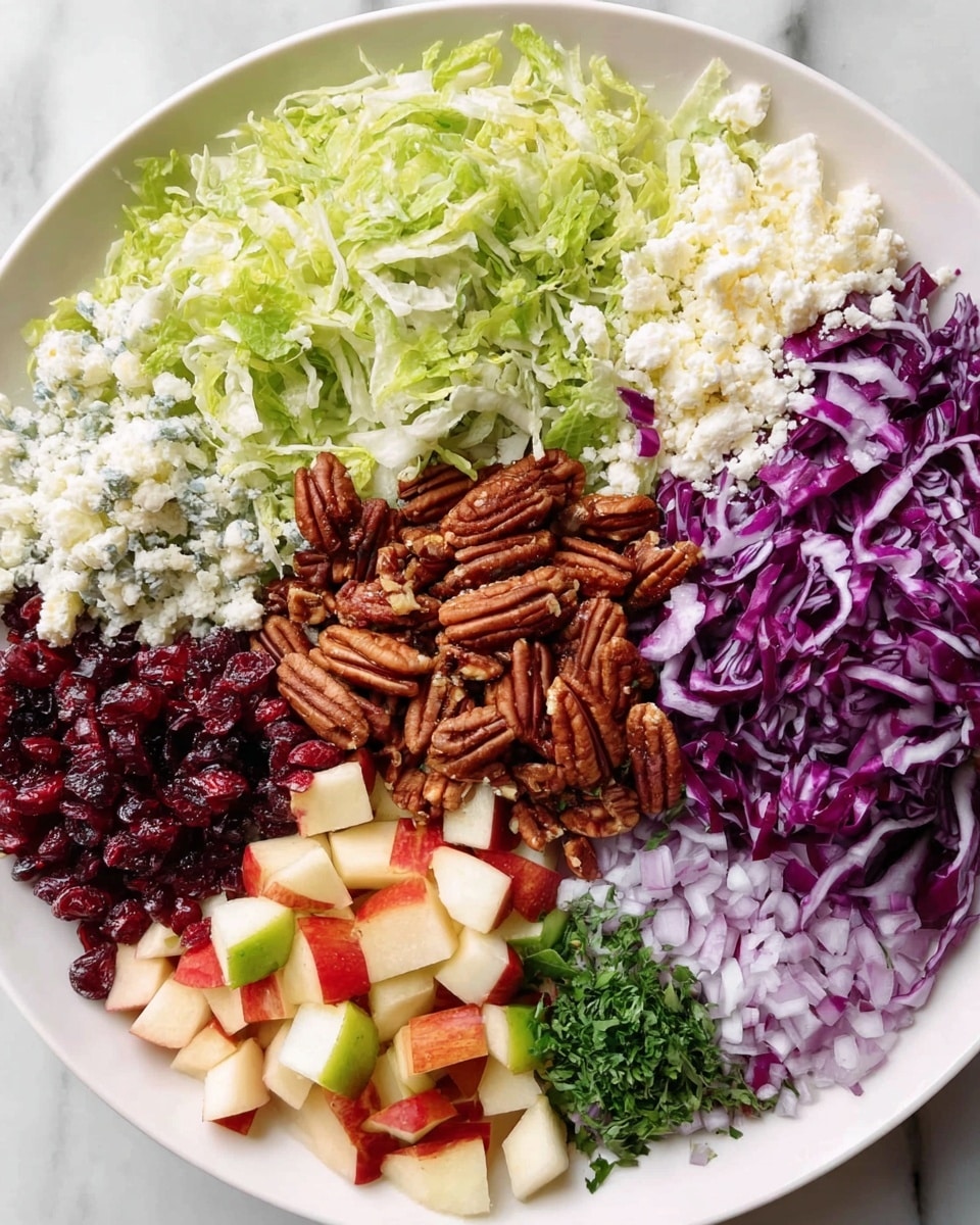 The image shows a white plate on a white marbled surface, filled with a colorful salad made of several distinct layers. Starting from the top left, there is a layer of light green shredded lettuce that looks fresh and crisp. Next to it on the right is a layer of finely crumbled white cheese, and beside that is a layer of thinly sliced deep purple cabbage with white veins. In the center sits a large pile of brown pecans with a rough texture. To the bottom right of the pecans is a scattered layer of small dried red cranberries mixed with small cubes of red and white apple. Below the apple pieces is a small bunch of finely chopped green herbs, and next to it at the bottom left is a small pile of finely chopped light purple onions. The colors and textures are very clear and fresh. Photo taken with an iphone --ar 4:5 --v 7