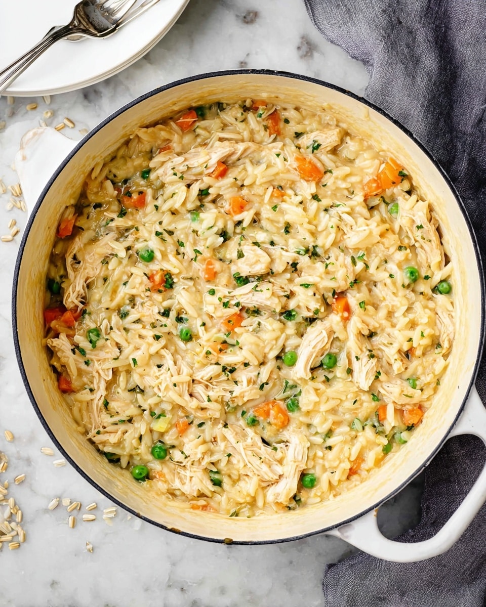 A white pot filled with a creamy mixture of shredded light-colored chicken, small green peas, and small orange carrot pieces mixed throughout a soft, rice-like or orzo texture, all coated in a pale yellow creamy sauce with small green herb pieces sprinkled on top. The pot rests on a white marbled surface with some uncooked grains scattered nearby and a folded grey cloth partially visible. A small part of a white plate and a fork are seen above the pot. photo taken with an iphone --ar 4:5 --v 7