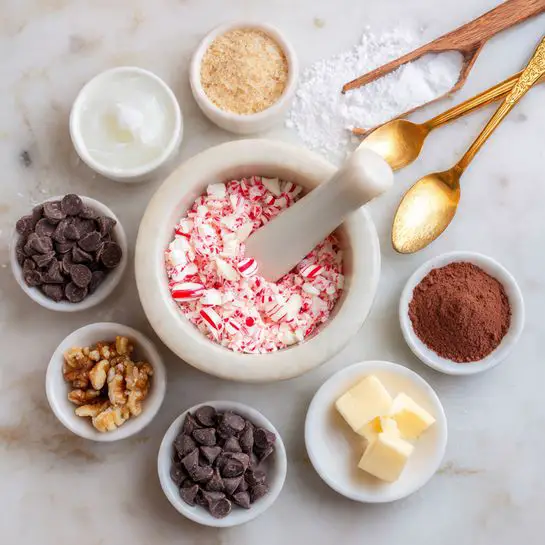 A white mortar and pestle filled with broken red and white peppermint candies sits at the center of the image on a white marbled surface. Surrounding it in a circle are small white and white-marble bowls containing various ingredients: white solid coconut oil, light brown crushed nuts, dark brown cocoa powder, white powder, golden brown sugar, and dark chocolate chips. Two wooden spoons lay diagonally above the mortar, one with a white powdery substance and the other with salt. A gold spoon rests on a white plate next to the bowls. The overall look is light and clean with a soft natural light. photo taken with an iphone --ar 4:5 --v 7
