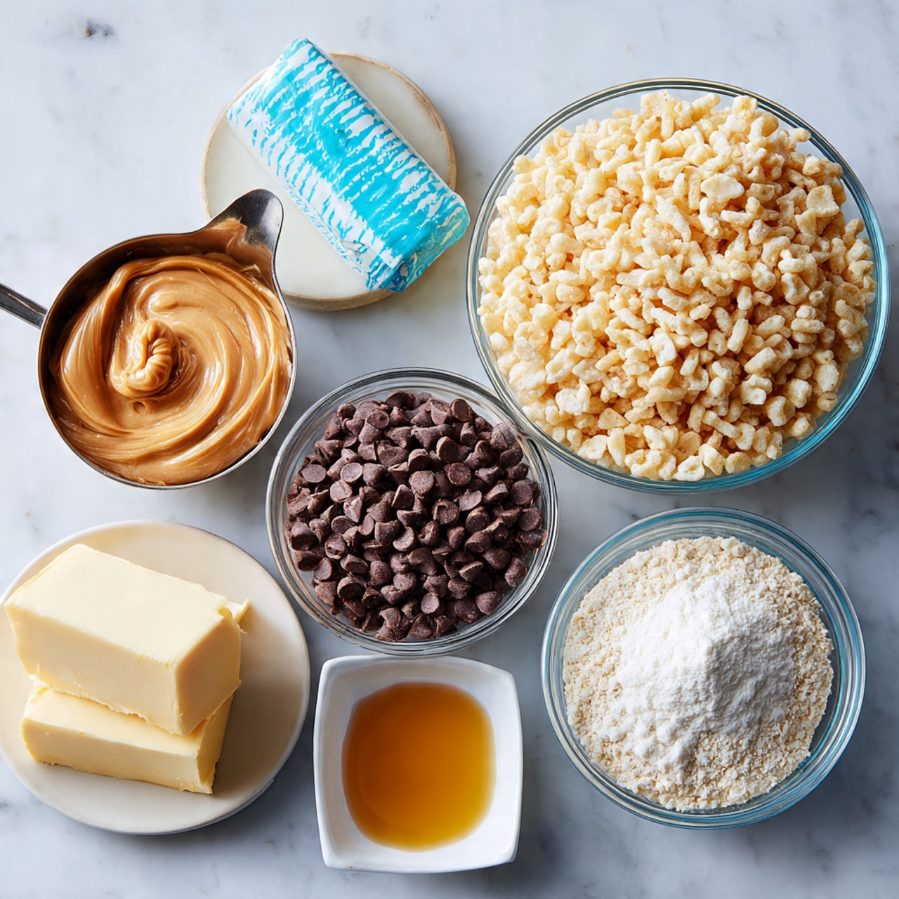 The image shows six ingredients placed neatly on a white marbled surface. There are two clear glass bowls, one filled with light beige puffed rice cereal and the other with dark brown chocolate chips. Above these bowls is a small stick of butter wrapped in blue and white paper. To the left, there is a half cup of smooth, light brown peanut butter in a silver measuring cup, a small square white dish holding golden vanilla extract, and a medium clear glass bowl filled with fine white powdered sugar. The arrangement is clean and simple, focusing on the texture and color contrast of the ingredients. Photo taken with an iphone --ar 4:5 --v 7