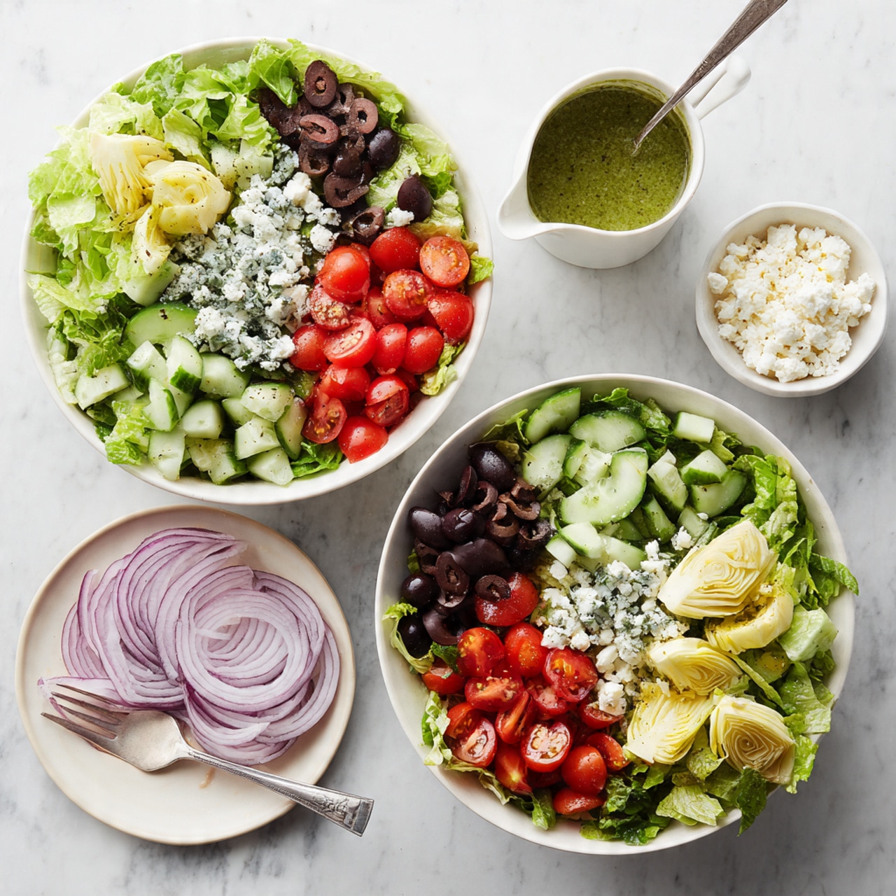 The image shows two white bowls filled with salad on a white marbled background. Each bowl has a base layer of bright green chopped lettuce. On top of the lettuce in both bowls, there are chopped cucumber pieces, halved red cherry tomatoes, and sliced black olives arranged in separate sections around the bowls. Next to the bowls, there is a small white bowl filled with crumbled white cheese and another white bowl with quartered artichoke hearts that are light yellow-green. Also placed near the bowls is a small white pitcher with green dressing, and a silver spoon is inside the pitcher. A few thin slices of red onion are arranged on a white plate to the left. Photo taken with an iphone --ar 4:5 --v 7