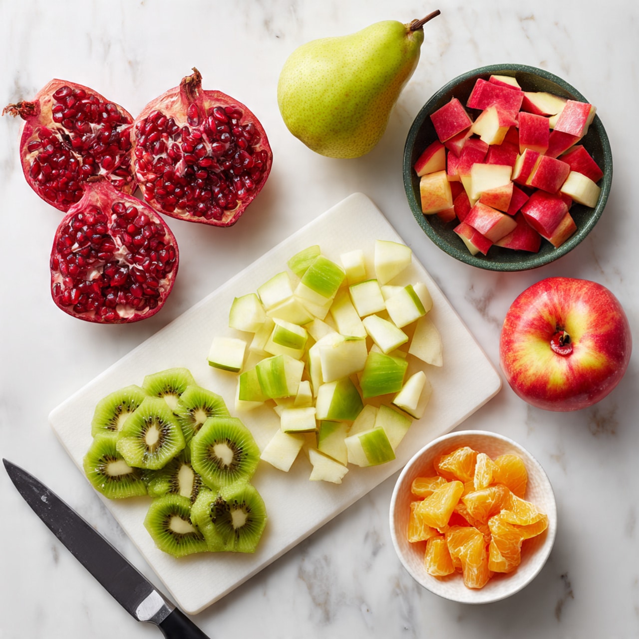 The image shows a preparation scene with different fresh fruits on a white marbled surface. There is a white cutting board in the center with half and quarter pomegranates showing bright red seeds on the left side. On this board, sliced green kiwi pieces lie in the middle with their soft texture visible. Above the board, a whole light green pear is placed. To the right, there is a dark green cutting board holding diced light green pear and red apple pieces. In the bottom right corner, half a red apple with a yellow spot at the core is placed next to a small bowl filled with orange fruit chunks. A black and silver knife rests at the bottom of the white board. Photo taken with an iphone --ar 4:5 --v 7