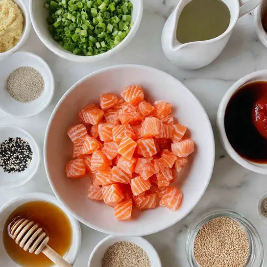 A large white bowl filled with many bright orange chunks of raw salmon with visible white lines, placed near the center right of the image. Surrounding the bowl are 9 small white bowls or containers arranged in a loose circle, each holding different ingredients: chopped green onions with shades of light and dark green at the top left, a roughly mashed pale yellow paste in the top center, a dark brown liquid in a small white pitcher at the top right, a thick red sauce in a bowl near the middle left, a honey-colored liquid with a wooden honey dipper resting in it just below the red sauce, a very small bowl with a dark brown liquid in the bottom center left, a small bowl with a mix of salt and black pepper at the bottom left, a bowl with light beige sesame seeds at the bottom center right, a bowl containing light brown powdered spices, and a small glass container with a clear liquid nearby. All is set on a white marbled surface photo taken with an iphone --ar 4:5 --v 7