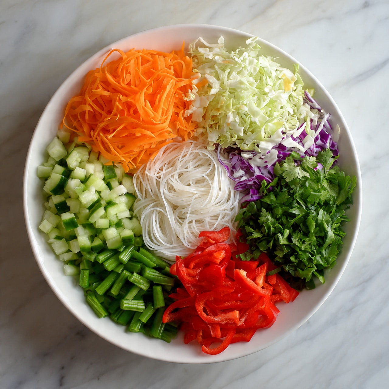 A large white bowl filled with six colorful layers of fresh vegetables and noodles, arranged neatly side by side. Starting from the top, there is a pile of thin, bright orange carrot ribbons with a smooth texture. To the right, a heap of shredded cabbage mix in white, light purple, and small orange bits adds a soft, leafy look. Below this, three small bunches of fine, white rice noodles sit with a delicate, tangled texture. Moving clockwise, bright red thin strips of bell pepper create a sharp contrast. Next, a pile of chopped green beans with a crisp, firm texture sits beside a pile of fresh cucumber slices, each bright green with light, watery centers. Finally, a mix of finely chopped green leafy herbs adds a vibrant finish near the carrots. The bowl rests on a white marbled surface, and the scene is lit with natural light. photo taken with an iphone --ar 4:5 --v 7