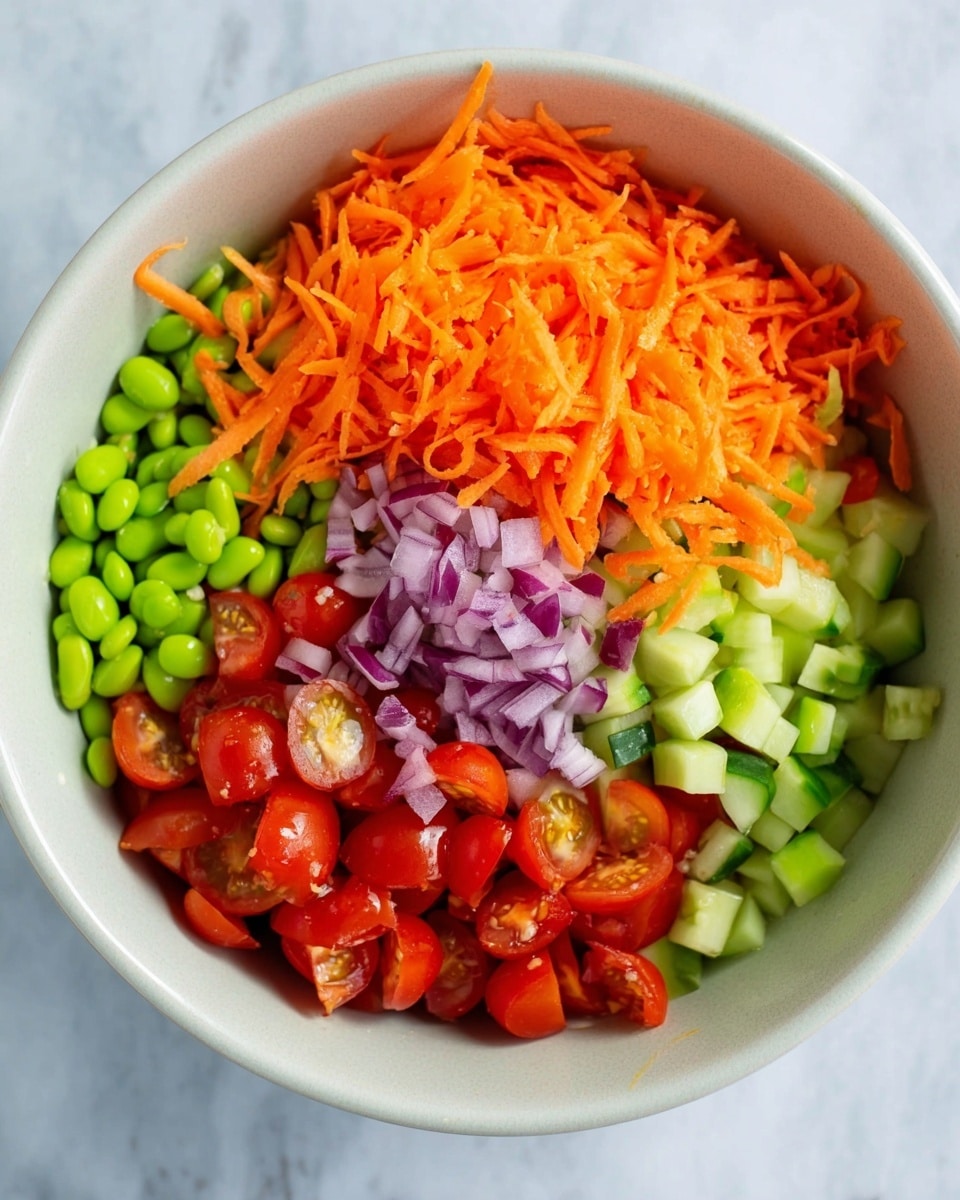 A large white bowl on a white marbled surface holds a colorful mix of fresh vegetables arranged in layers. The bottom layer is bright green edamame beans, next to a layer of halved red cherry tomatoes mixed with light green cucumber pieces. Above these is a layer of finely chopped purple onion, topped with a generous pile of shredded orange carrot. The textures range from smooth and shiny edamame, to juicy and slightly glossy tomatoes, to the rough, fluffy look of freshly shredded carrot. photo taken with an iphone --ar 4:5 --v 7