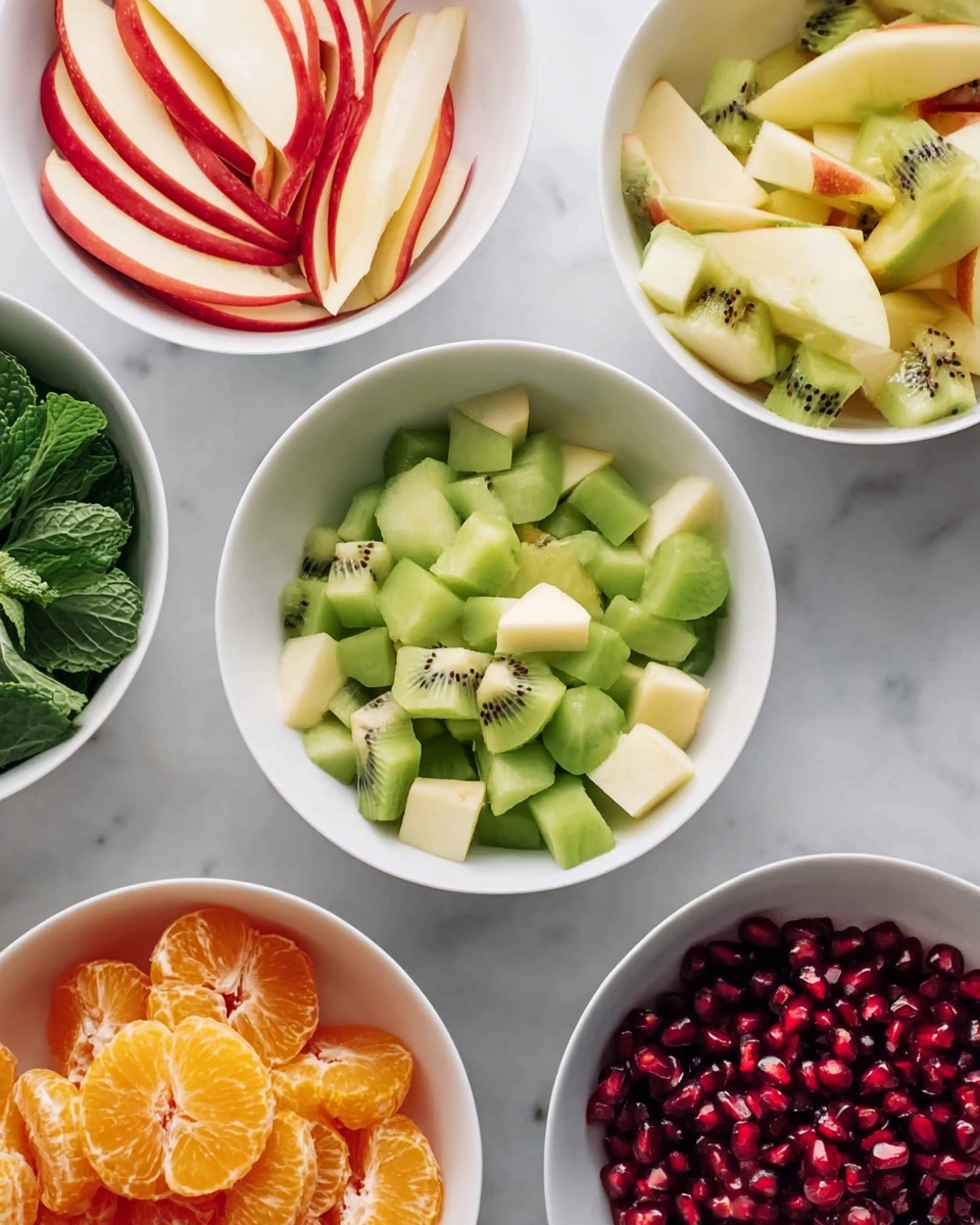 The image shows five white bowls arranged on a white marbled surface, each filled with a different type of fruit. One bowl contains thin slices of red apple with light cream flesh. Another bowl is filled with bright green kiwi pieces, cut into small chunks with visible black seeds. There is a bowl with small orange tangerine segments, peeled and glossy. A fourth bowl holds small, cubed pieces of greenish-yellow pear with its skin still on some pieces. The final bowl is filled with deep red pomegranate seeds, densely packed. In the top left corner, fresh green mint leaves are visible on the surface. photo taken with an iphone --ar 4:5 --v 7
