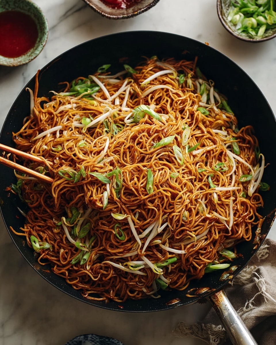 A black textured round plate holds a large serving of thin, golden-brown stir-fried noodles mixed with light beige bean sprouts and green onion pieces scattered throughout. The noodles have a slight shine and some crispy bits, showing a mix of smooth and crunchy textures. Brown wooden chopsticks rest on the right edge of the plate. The scene is set on a white marbled surface with a small bowl of sliced green onions nearby. photo taken with an iphone --ar 4:5 --v 7