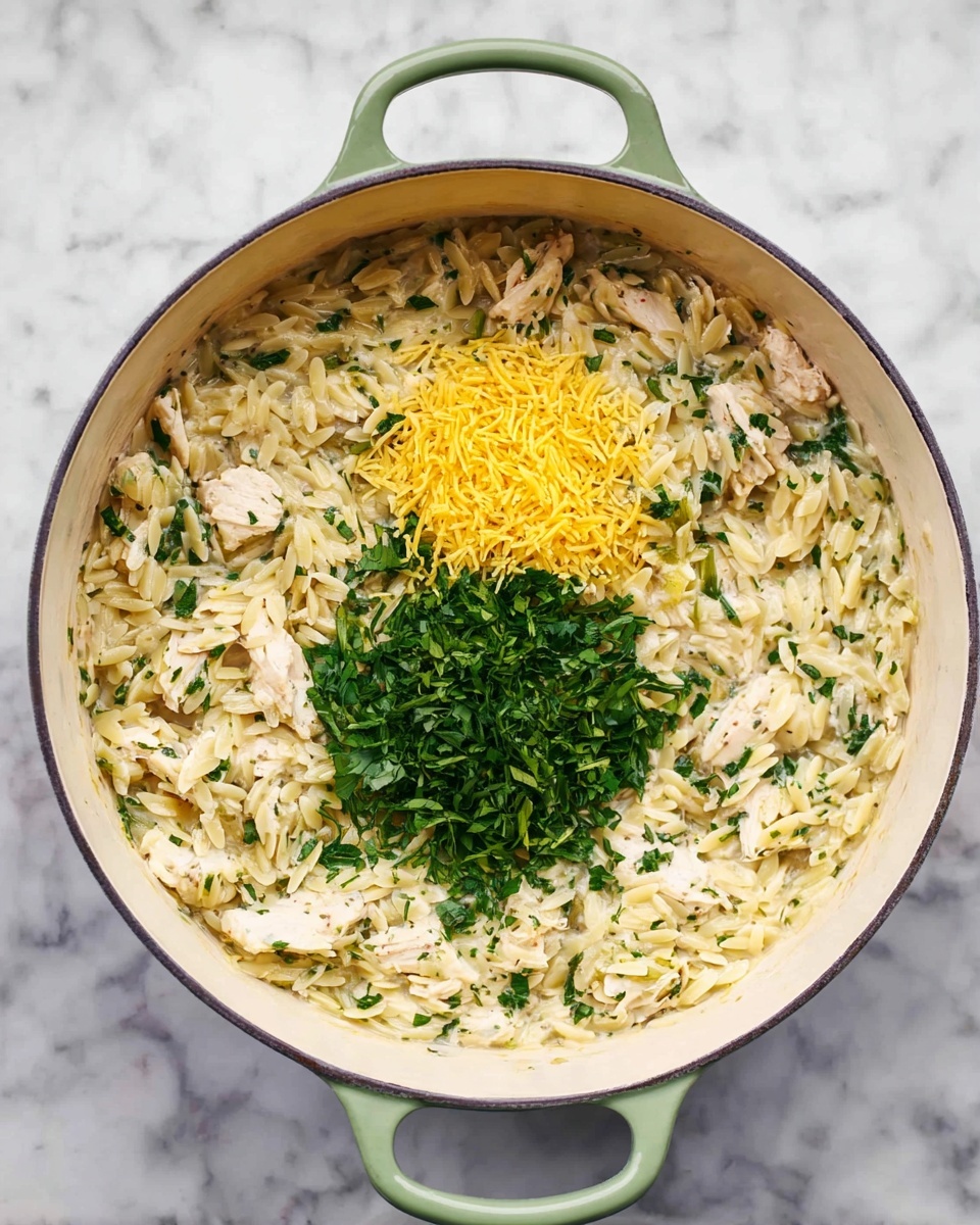 A round white cooking pot with light green handles holds a creamy orzo pasta dish mixed with small pieces of chicken and chopped green herbs. The orzo is off-white with a soft texture, mixed evenly throughout the pot. In the center, two distinct piles sit on top: one bright yellow, finely grated, and another made of fresh leafy green herbs, creating a contrast against the creamy pasta below. The pot is placed on a white marbled surface. photo taken with an iphone --ar 4:5 --v 7