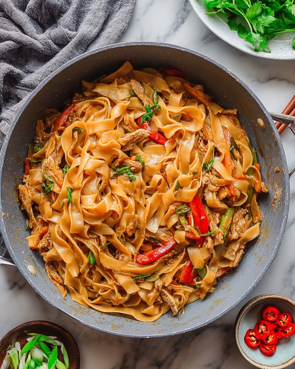 A large gray pan filled with wide, flat noodles coated in a glossy light brown sauce, mixed with thin strips of cooked light beige meat scattered throughout. There are slices of red bell pepper and bright green herbs and spring onions mixed in, adding touches of red and green colors. The pan sits on a white marbled surface with a gray cloth on the upper left, a white plate with fresh green herbs on the upper right, and small bowls with sliced green onions and red chili peppers near the bottom. photo taken with an iphone --ar 4:5 --v 7