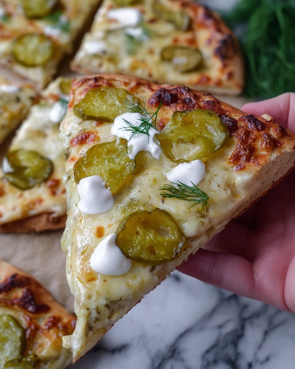 A slice of pizza is held by a woman's hand, showing three layers: the thin crust with a light golden-brown edge, a melted cheese layer with golden spots on top, and rings of green pickles scattered across the cheese. There are small dollops of white sauce drizzled over the slice with a few tiny green herb sprigs, likely dill, adding color. The background shows more pizza slices on a white marbled surface with fresh dill sprigs nearby. photo taken with an iphone --ar 4:5 --v 7