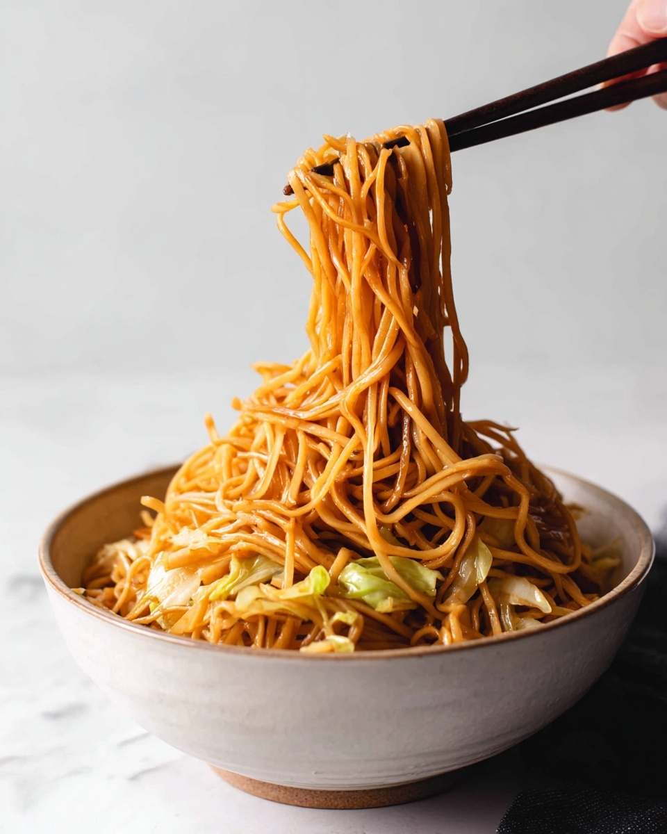 Panda Express Chow Mein Recipe 5 A close-up view of a bowl filled with thin orange-brown noodles mixed with small pieces of light green cabbage. The noodles are lifted in the air by a pair of dark chopsticks held by a woman's hand, showing their long and soft texture. The bowl is white with a simple design and sits on a white marbled surface. The background is softly lit and plain, keeping the focus on the noodles and their shiny, slightly glossy look. Photo taken with an iphone --ar 4:5 --v 7