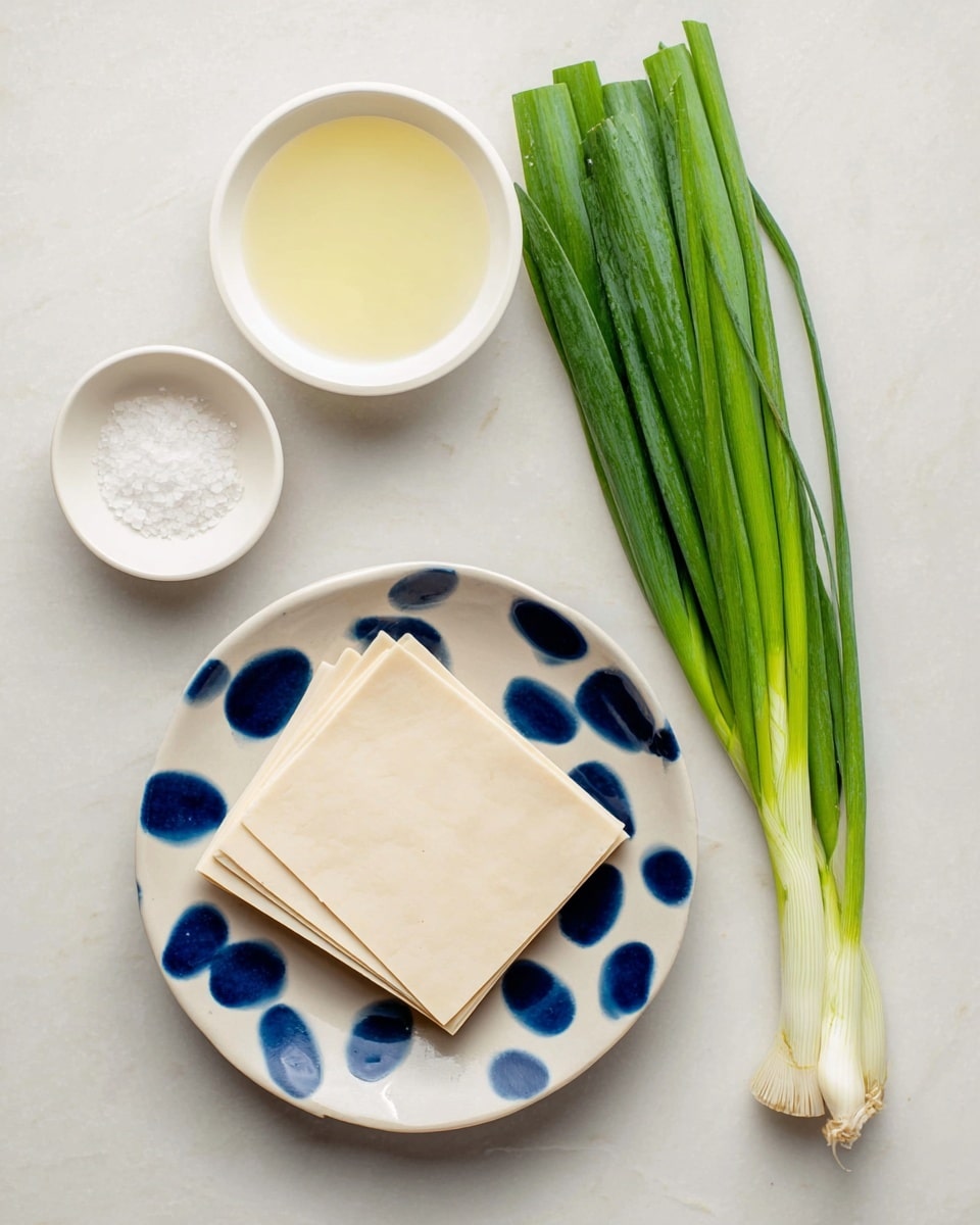 A white plate with blue spots holds a neat stack of thin, square light beige sheets, placed at the bottom right corner. To the upper left of the plate, a bunch of fresh green scallions lies diagonally, showing smooth green leaves and whitish roots. Above the scallions, there are two small white bowls; the bigger one contains a pale yellow liquid, and the smaller one holds a pile of white granulated salt. All items rest on a clean white marbled surface. Photo taken with an iphone --ar 4:5 --v 7