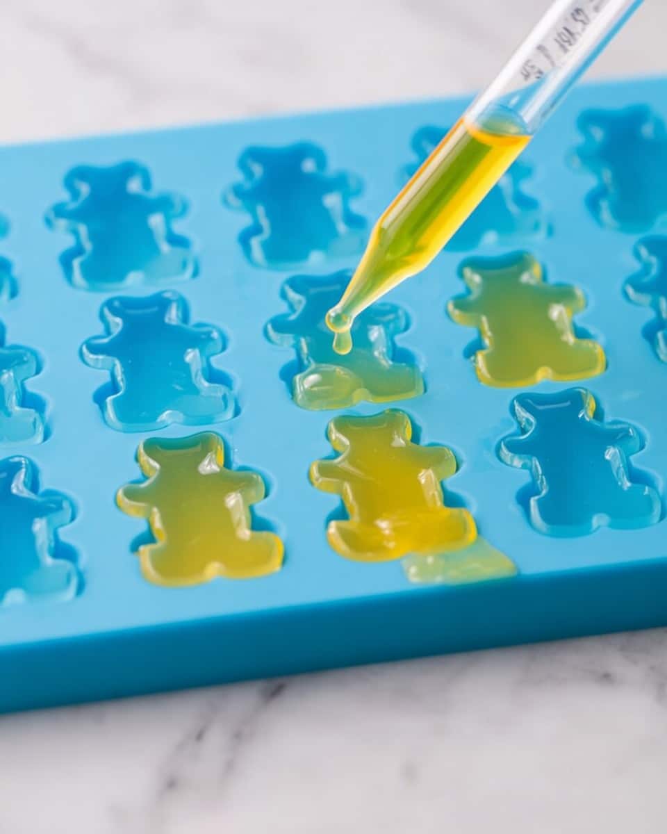 A close-up image shows a blue silicone mold shaped like small bears filled partially with a yellow liquid. A clear dropper with yellow liquid is being used to fill one of the bear-shaped cavities. Some of the cavities are already filled with the yellow liquid, which has a smooth, shiny texture. The blue mold rests on a white marbled surface, with parts of the yellow liquid spilled around the mold edges. photo taken with an iphone --ar 4:5 --v 7
