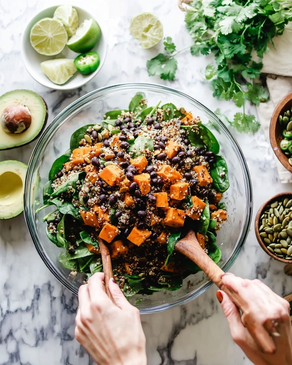 A large clear glass bowl filled with a colorful salad showing three main layers: a base layer of dark green spinach leaves, a middle layer of black beans scattered throughout, and a top layer of roasted orange sweet potato cubes mixed evenly with light-colored quinoa. Two woman's hands are mixing the salad using wooden spoons. The bowl sits on a white marbled surface surrounded by fresh ingredients including a halved avocado with the seed inside, a white small bowl with lime wedges, some green jalapeño peppers, cilantro leaves, and a white bowl filled with pumpkin seeds. Photo taken with an iphone --ar 4:5 --v 7