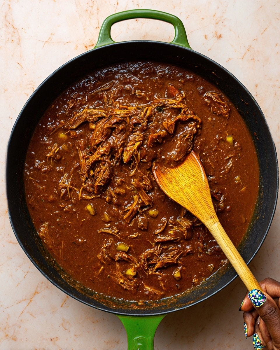 A close-up photo of a black pan with a green handle filled with rich, brown stew. The stew has visible shredded meat and small chunks of vegetables mixed deeply in a thick sauce with a smooth texture. A wooden spoon is resting in the pan, partly dipped in the stew, showing some glossy shine on the sauce. A woman's hand with decorated nails is holding the green pan handle at the bottom. The background is a white marbled texture. photo taken with an iphone --ar 4:5 --v 7
