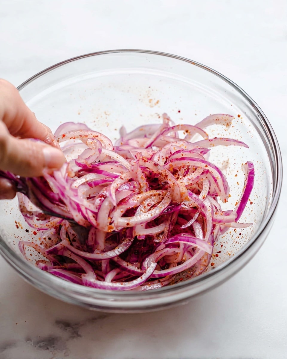 A clear glass bowl sits on a white marbled surface, filled with thinly sliced red onions mixed with specks of red seasoning. The onions are light purple with a shiny, slightly wet texture. A woman's hand is gently mixing the onions inside the bowl, adding a natural and fresh feel to the scene. The inside of the bowl shows some fine splashes of red seasoning, highlighting the spreading of flavors. photo taken with an iphone --ar 4:5 --v 7