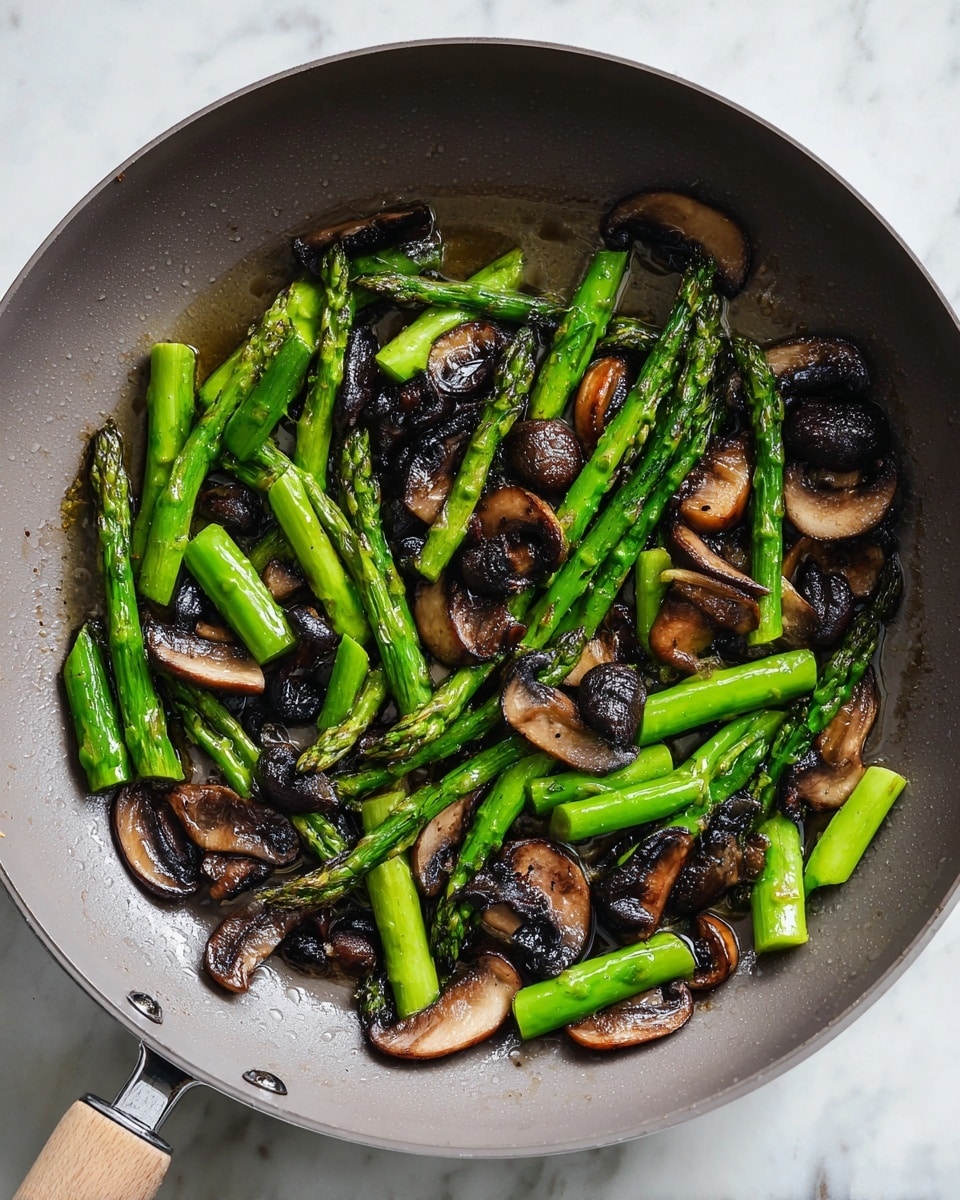 A gray pan holds a mix of cooked vegetables arranged in one visible layer: bright green asparagus pieces, each about two to three inches long with a glossy cooked texture, and dark brown sliced mushrooms that appear soft and slightly shiny. The asparagus is thick and firm, some pieces slightly charred, while the mushroom slices vary in size and show a gentle curve. The pan’s inside surface is smooth, and small drops of oil are scattered around the vegetables. The pan sits on a white marbled surface. Photo taken with an iphone --ar 4:5 --v 7