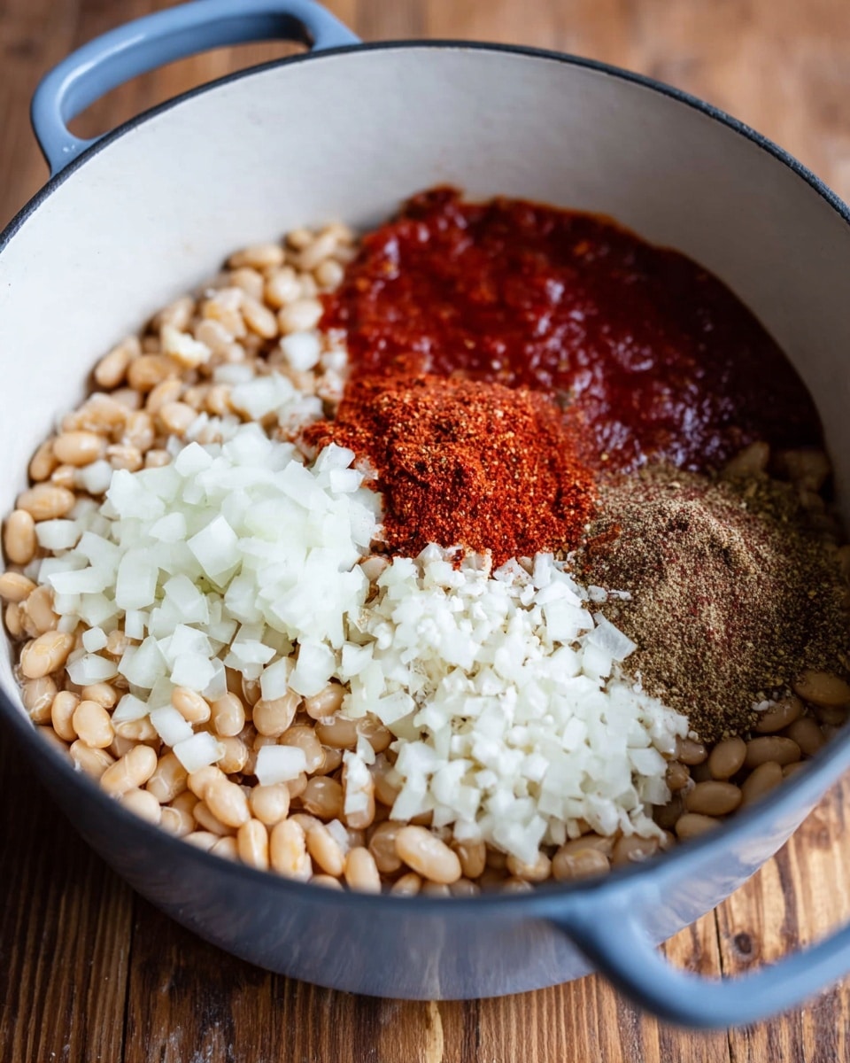 A close-up image shows a white pot filled with several distinct layers of ingredients. The base layer consists of small, beige beans covering the bottom. On top of that, there are four separate piles arranged close together: finely chopped white onions on the right, a dark brown powder or spice mix next to the onions, a thick, bright red sauce behind the onions and spices, and a small amount of additional sauce or seasoning adjacent to the red sauce. The pot is placed on a wooden surface but the visible background and surface around it should be imagined as a white marbled texture. Photo taken with an iphone --ar 4:5 --v 7