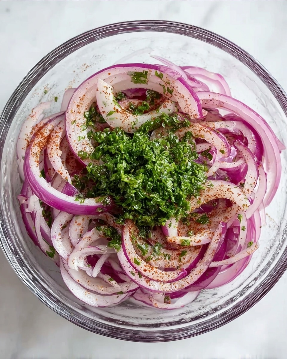 A clear glass bowl holds thinly sliced rings of purple and pale pink onion, mixed with a light dusting of reddish-brown spice. On the top center, there is a small pile of finely chopped fresh green herbs, adding a vibrant contrast. The bowl sits on a white marbled surface. photo taken with an iphone --ar 4:5 --v 7