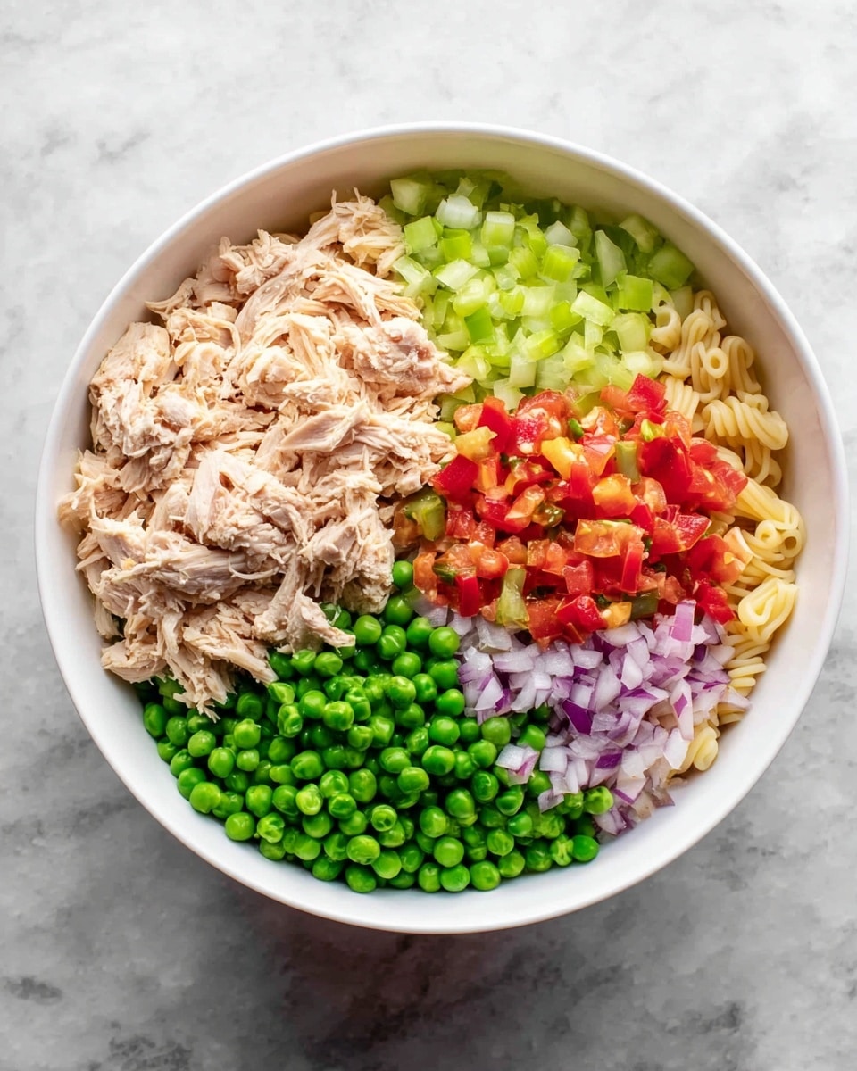 A white bowl sits on a white marbled surface filled with five distinct layers of ingredients. On the top left is a pile of light beige shredded chicken, next to it on the right is a mix of small chopped red bell pepper and celery pieces in light green and red colors. Below this mixture, finely chopped pale purple onions add a splash of color. On the bottom left, bright green peas are placed, and next to them, pale yellow elbow pasta forms the base layer visible around the edges. The colors and textures offer a fresh, raw look with clear separation between each ingredient. photo taken with an iphone --ar 4:5 --v 7