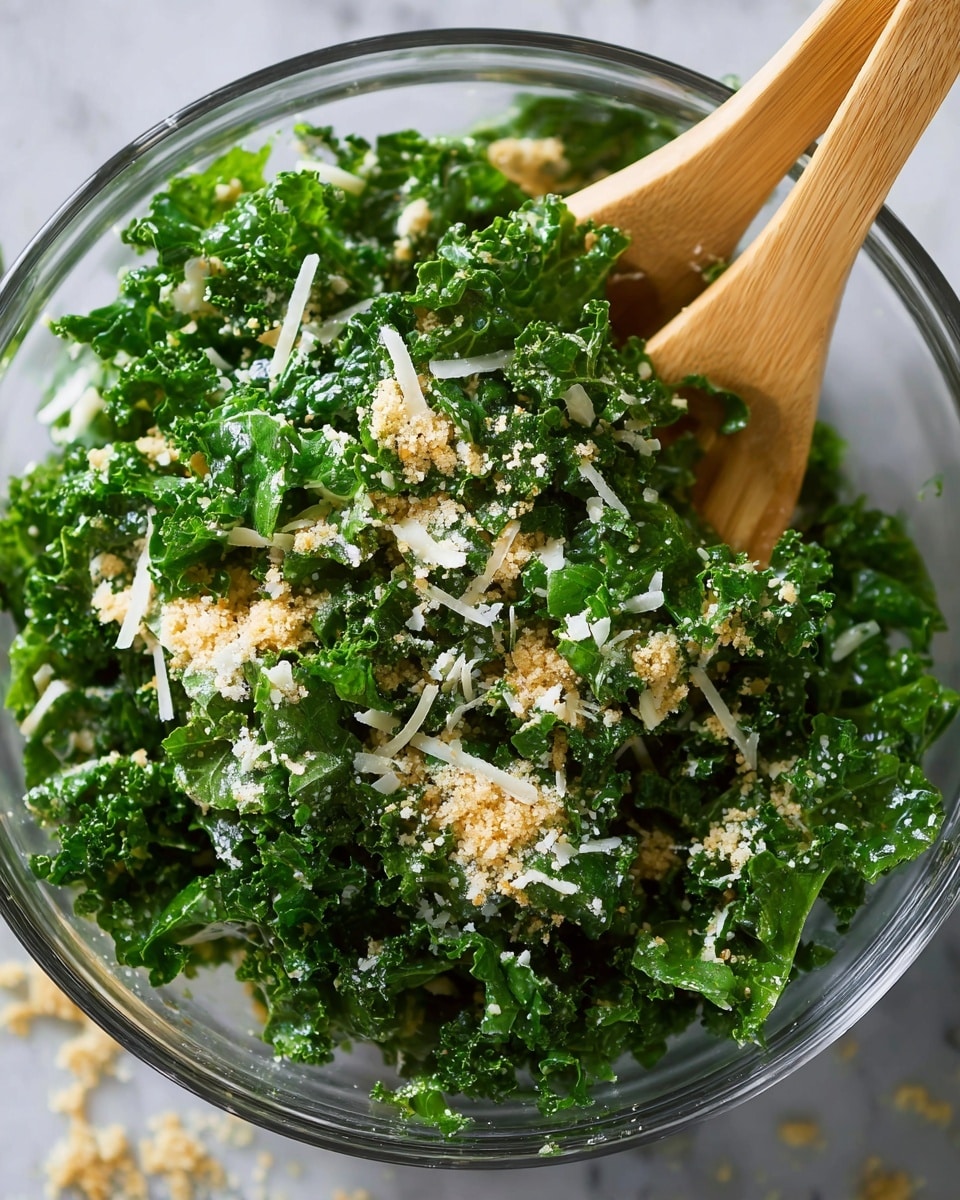 A clear glass bowl filled with bright green, curly kale leaves that look fresh and slightly shiny, mixed with small white shredded cheese pieces and light golden bread crumbs spread evenly on top and throughout the salad. Two light wooden salad forks rest diagonally inside the bowl, partially covered by the kale. The bowl sits on a white marbled textured surface with some crumbs scattered around. photo taken with an iphone --ar 4:5 --v 7