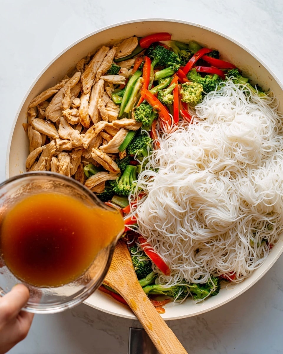 A white pan on a white marbled surface holds three layers: on the left, light brown cooked strips of chicken; below them, bright green broccoli and sliced green and red bell peppers; on the right, a large pile of soft, white rice noodles. A woman's hand pours a shiny brown sauce from a clear glass bowl into the pan, while a wooden spatula rests on the edge. The colors are bright and fresh, showing a mix of textures and tones. Photo taken with an iphone --ar 4:5 --v 7