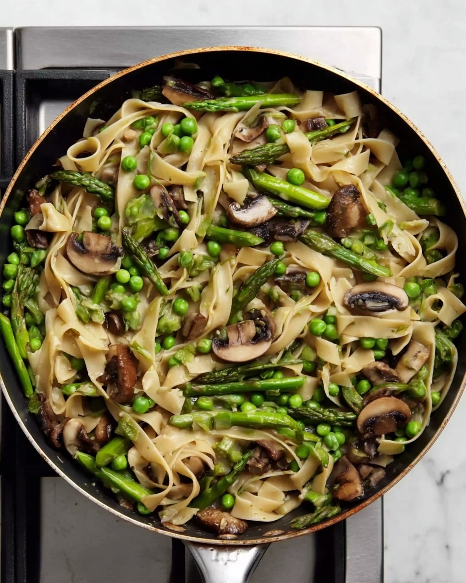 A close-up top view of a black pan filled with cooked wide flat noodles mixed with green peas, bright green asparagus pieces, and sliced brown mushrooms. The flat noodles create a creamy beige base layer, interwoven with the fresh green veggies and tender mushrooms spread evenly throughout. The pan rests on a white marbled surface with a stainless steel stove burner partially visible around the edges. The overall look is fresh and natural with earthy tones from the mushrooms and vibrant green colors from the vegetables, showing a simple vegetable noodle stir-fry. photo taken with an iphone --ar 4:5 --v 7