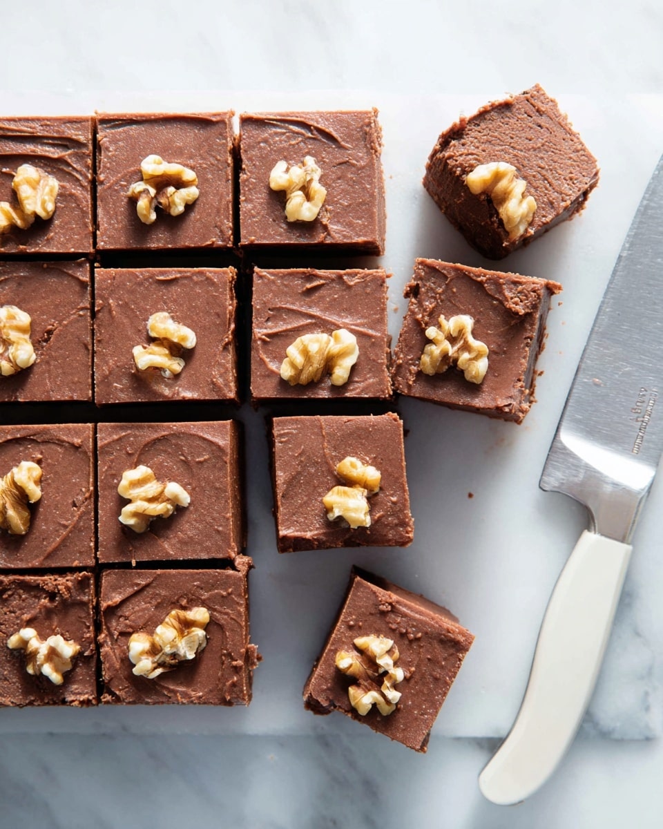 The image shows a group of square pieces of chocolate fudge with walnuts on top, arranged neatly on a white marbled surface. The fudge is cut into three rows and four columns, with three pieces slightly pulled out on the right side, showing their thick, dense texture with a rich brown color. Each piece has one or two walnut halves pressed into the smooth top layer, adding texture and a light beige contrast to the dark chocolate. A large knife with a white handle lies nearby on the right side, suggesting the fudge was freshly sliced. Photo taken with an iphone --ar 4:5 --v 7
