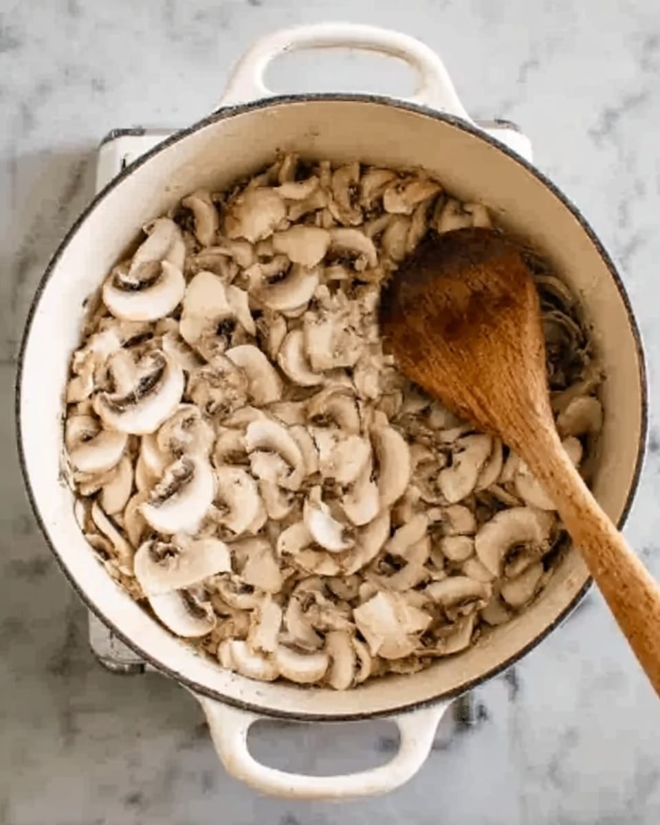The image shows a white pot filled with thinly sliced mushrooms cooking inside. The mushrooms are light brown and beige with a soft texture, spread evenly across the pot. There is a wooden spoon placed inside the pot on the right side, stirring the mushrooms. The pot sits on a stovetop with a white marbled surface around it. The photo has a clear top-down view, making it easy to see the mushrooms and the wooden spoon. Photo taken with an iphone --ar 4:5 --v 7