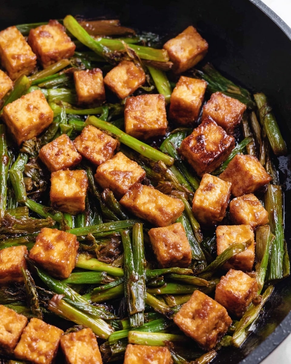 The image shows a black pan filled with small cubes of golden brown tofu mixed with green roasted scallions. The tofu pieces have a crispy texture with a warm caramel color, scattered evenly throughout the pan. The scallions are roasted, appearing slightly wrinkled and charred, adding a darker green and brown contrast to the bright tofu cubes. The pan's interior is smooth and dark, making the vibrant colors of the tofu and scallions stand out clearly. photo taken with an iphone --ar 4:5 --v 7