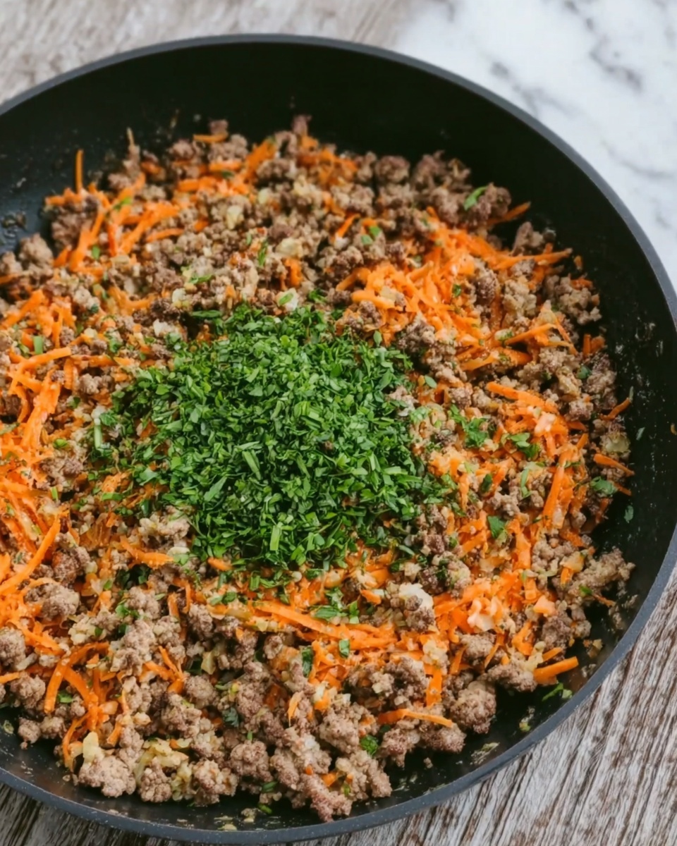 The image shows a black pan filled with cooked ground meat mixed with small strips of orange carrot evenly spread throughout. In the center, there is a pile of finely chopped green herbs adding a fresh color contrast. The texture of the meat looks crumbly but moist, and the carrots appear tender. The pan rests on a white marbled surface. photo taken with an iphone --ar 4:5 --v 7