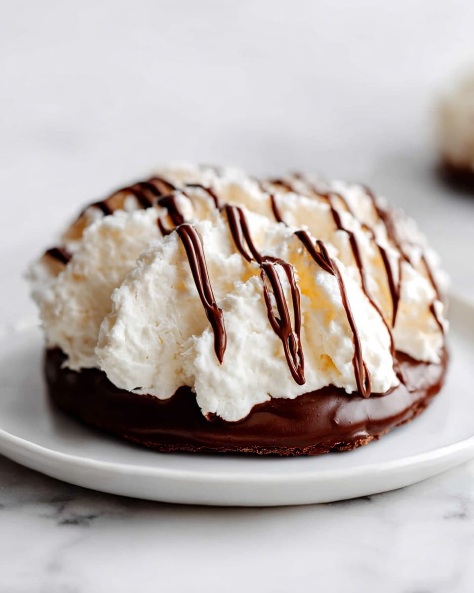 The image shows a single dessert with two main layers. The bottom layer is a thick, dark brown chocolate base that spreads wide and looks smooth. On top of it is a fluffy, white, textured layer that looks like whipped meringue or coconut. The white layer has a soft, uneven surface with peaks and ridges, giving it a light and airy look. Drizzled over the white layer are thin lines of dark chocolate that zigzag from one side to the other, creating a striped pattern. The dessert is placed on a white plate set on a white marbled surface. photo taken with an iphone --ar 4:5 --v 7