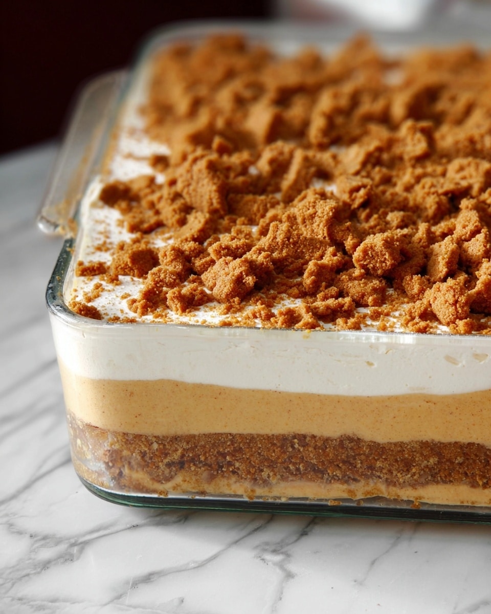 The image shows a close-up of a layered dessert in a clear rectangular glass dish set on a white marbled surface. The dessert has four layers: the bottom layer is a crumbly, golden brown crust; above it is a thick, creamy, light caramel-colored layer; next is a smooth, white layer that looks like whipped cream; and the top layer is sprinkled generously with crushed, crunchy brown cookie pieces. The focus is on the textures of the dessert, especially the crumbly bits on top. Photo taken with an iphone --ar 4:5 --v 7