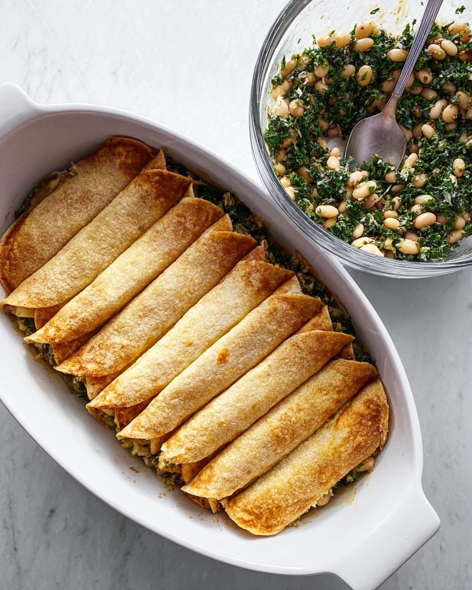 The image shows a white oval baking dish filled with 10 golden-brown folded tortillas lined up side by side, covering a dark green and white bean filling peeking out slightly at the edges; next to the dish is a clear glass bowl with a fresh mix of white beans, leafy greens, and herbs, with a silver spoon resting inside, all placed on a white marbled surface. photo taken with an iphone --ar 4:5 --v 7