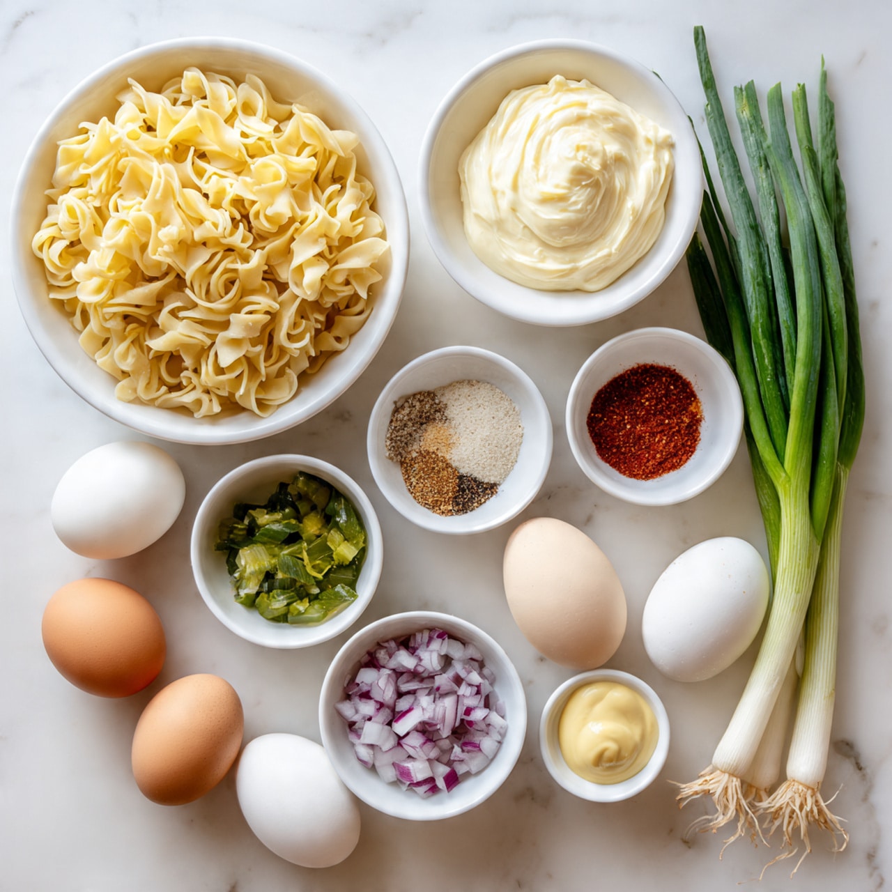 The image shows several white bowls and eggs arranged on a white marbled surface. A large white bowl holds curled yellow pasta in the top left. To its right, a medium white bowl is filled with creamy, pale yellow mayo. Below the mayo, a small white bowl contains a mix of spices in separate sections, showing light beige garlic powder, red paprika, white salt, and black pepper. Below the pasta bowl, a small white bowl holds chopped green pickles. In the lower right corner, a medium white bowl contains small purple and white chopped red onions. Next to the pickles, a tiny white bowl has smooth, light yellow dijon mustard. There are six eggs scattered in the center area, varying in color from white, pale green to brown. In the upper right corner, a bunch of long, green onions lies partially in the frame. The overall feel is clean and fresh. photo taken with an iphone --ar 4:5 --v 7