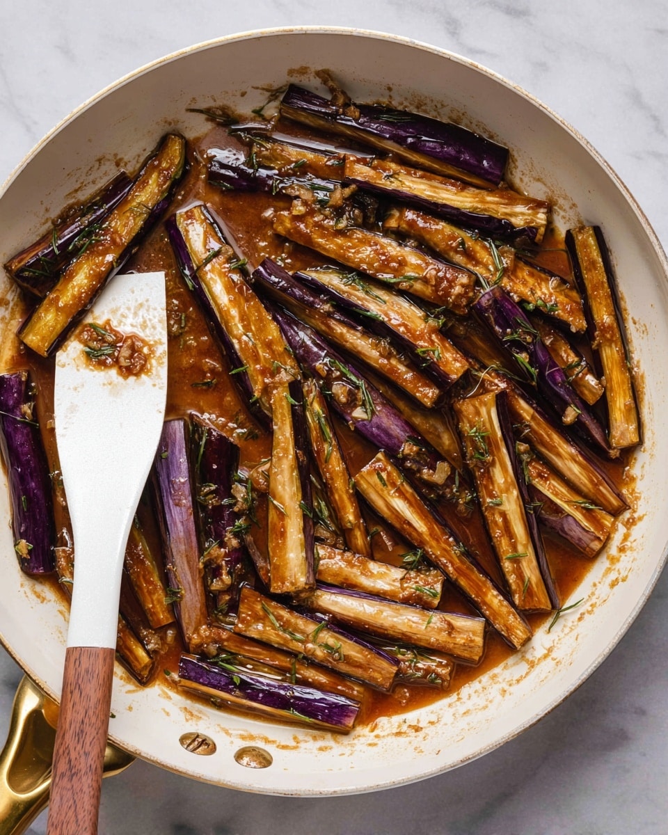 Inside a white pan with a golden handle, there are many long, thin pieces of cooked eggplant laid scattered. The eggplants have a mix of deep purple and light brown colors with a shiny, slightly wet surface from a thick brown sauce. The sauce also has small bits of minced garlic and green herbs spread unevenly across the eggplant pieces. A white spatula with a wooden handle rests on the left side of the pan, partly under some eggplant sticks. The background shows a white marbled surface. photo taken with an iphone --ar 4:5 --v 7