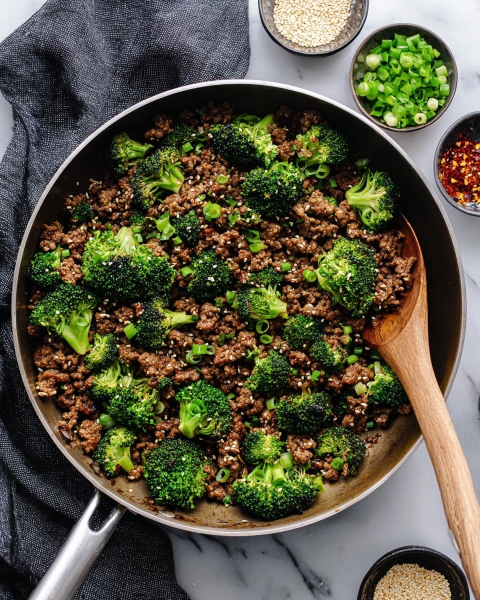 A large pan filled with a mixture of cooked ground meat and bright green broccoli florets. The ground meat is brown and has a slightly glossy texture, mixed evenly with fresh green broccoli pieces. There are small bits of green onions scattered on top and some white sesame seeds sprinkled over the dish. On the right side of the pan is a wooden spoon resting partially in the food. The pan sits on a white marbled surface with a dark gray cloth and small bowls containing sesame seeds, red pepper flakes, and chopped green onions placed nearby. Photo taken with an iphone --ar 4:5 --v 7