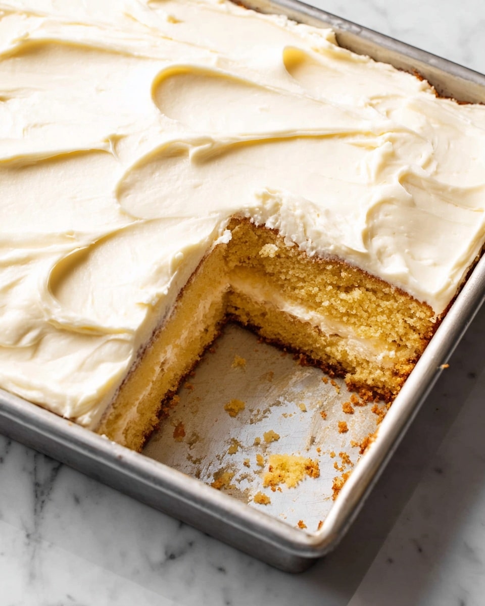 The image shows a rectangular metal baking pan with a creamy white frosting on top, spread smoothly but with soft wave-like textures. One corner section is missing, revealing two thick layers of yellow sponge cake beneath the frosting. The cake looks moist with a slightly crumbly texture. The bottom of the pan shows some leftover frosting and crumbs. The pan rests on a white marbled surface. photo taken with an iphone --ar 4:5 --v 7