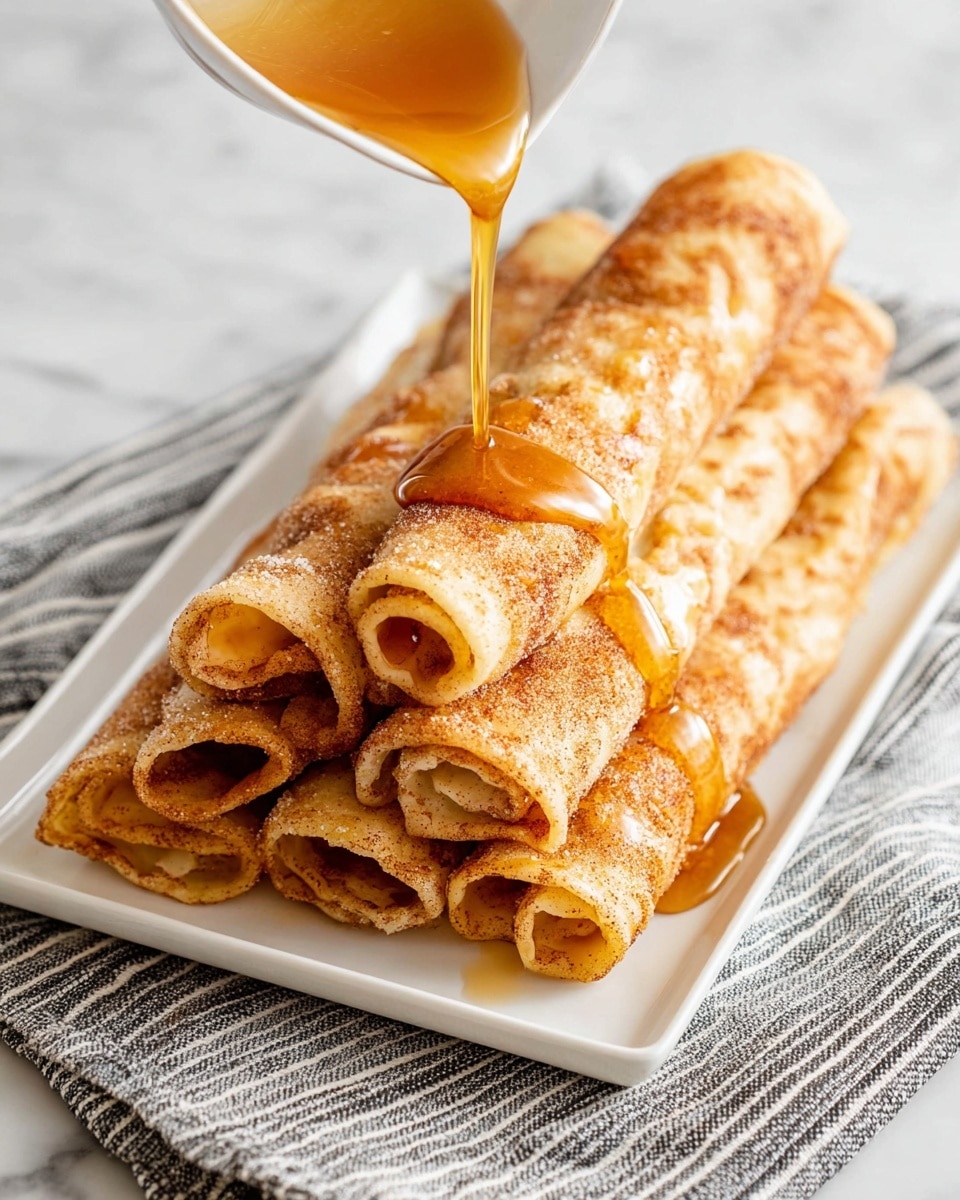 The image shows a stack of five rolled crepes on a white plate. Each crepe is golden brown with a slightly crispy texture and a light dusting of cinnamon sugar. The crepes are arranged in two layers, with three on the bottom and two on top, all drizzled with a light amber syrup that glistens under the light. The ends of the crepes reveal a soft, pale yellow filling inside. There is a silver fork resting on the left side of the plate. The plate sits on a white marbled surface. photo taken with an iphone --ar 4:5 --v 7