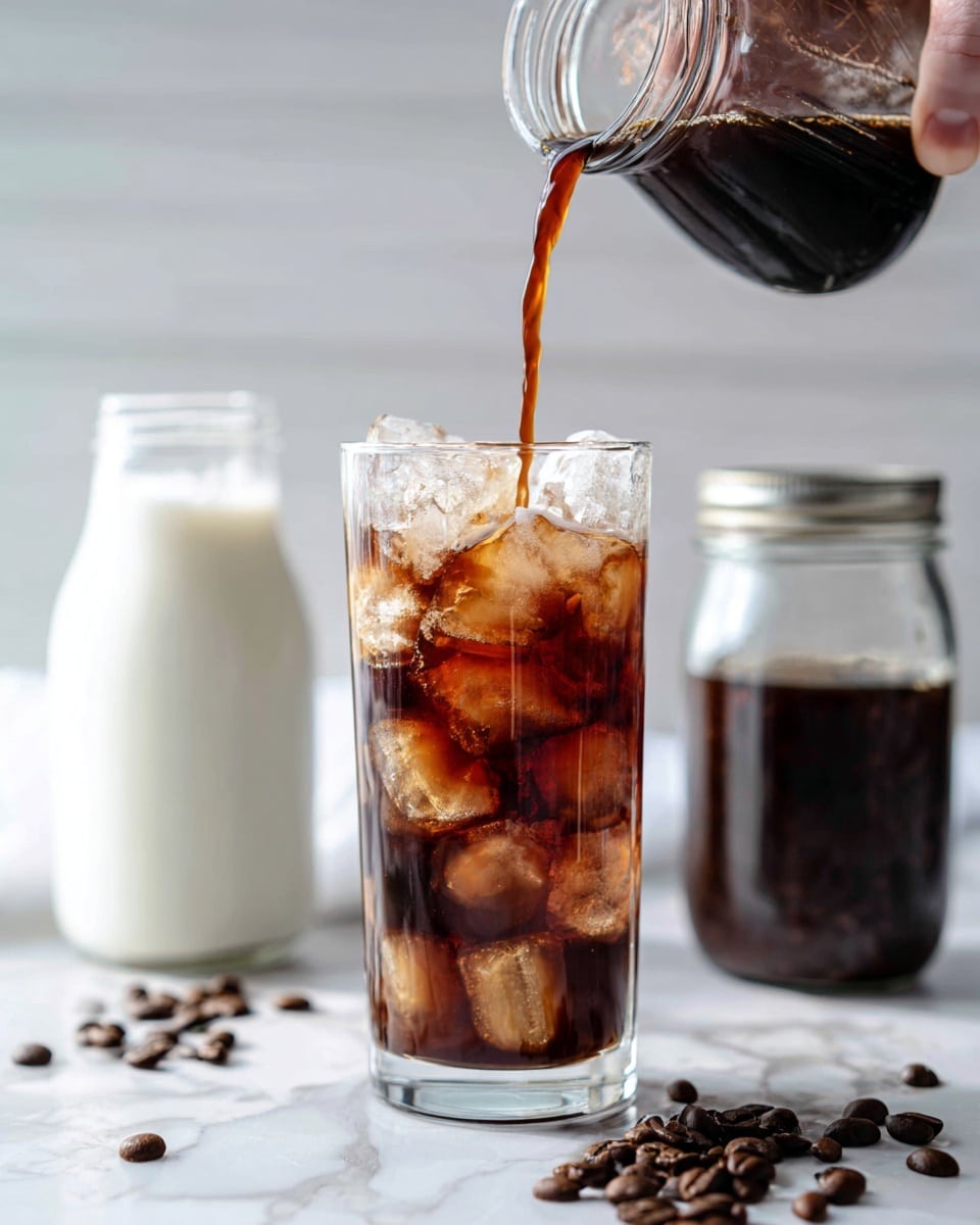 A tall clear glass filled with many ice cubes has dark brown cold coffee being poured into it from a small clear jar held by a woman's hand on the left side, the coffee swirls and splashes over the ice. Behind the glass, two jars are visible: one shorter white jar filled with white milk and one taller clear jar filled with dark coffee and topped with a metal lid. Brown coffee beans scatter on the white marbled surface in front of the glass. The background is bright and softly blurred with light gray and white horizontal lines. Photo taken with an iphone --ar 4:5 --v 7