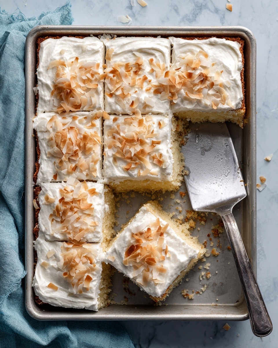 A rectangular silver baking pan holds six square cake pieces, with one piece missing in the top right corner. Each cake piece has two visible layers—the bottom layer is light golden brown and crumbly, while the top layer is a thick, smooth white frosting sprinkled lightly with toasted coconut flakes in light tan shades. A large metal spatula rests in the empty space, with some crumbs on it. The pan sits on a white marbled surface, with a soft blue-gray cloth partially visible at the bottom left corner. Photo taken with an iphone --ar 4:5 --v 7