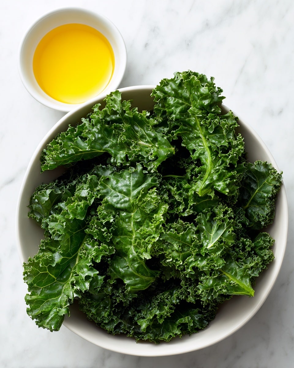 A white bowl filled with bright green curly kale leaves, showing their wavy and textured edges, is placed on a white marbled surface. Above the bowl, a small white bowl contains golden yellow extra virgin olive oil. The overall image is simple, highlighting the fresh, leafy green kale and the smooth, shiny olive oil in clean white bowls. Photo taken with an iphone --ar 4:5 --v 7